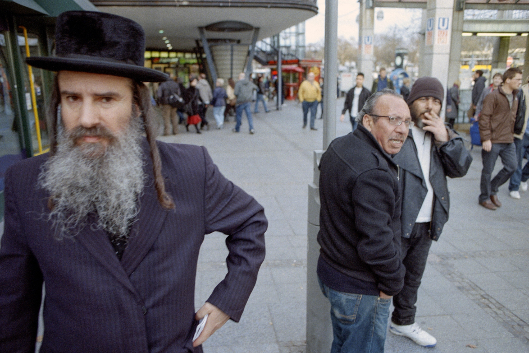 Ein orthodoxer Jude am Bahnhof "Zoologischer Garten" in Berlin Ein älterer Mann mit Hut, Bart und Schläfenlocken steht auf einem belebten Platz und blickt in die Kamera.